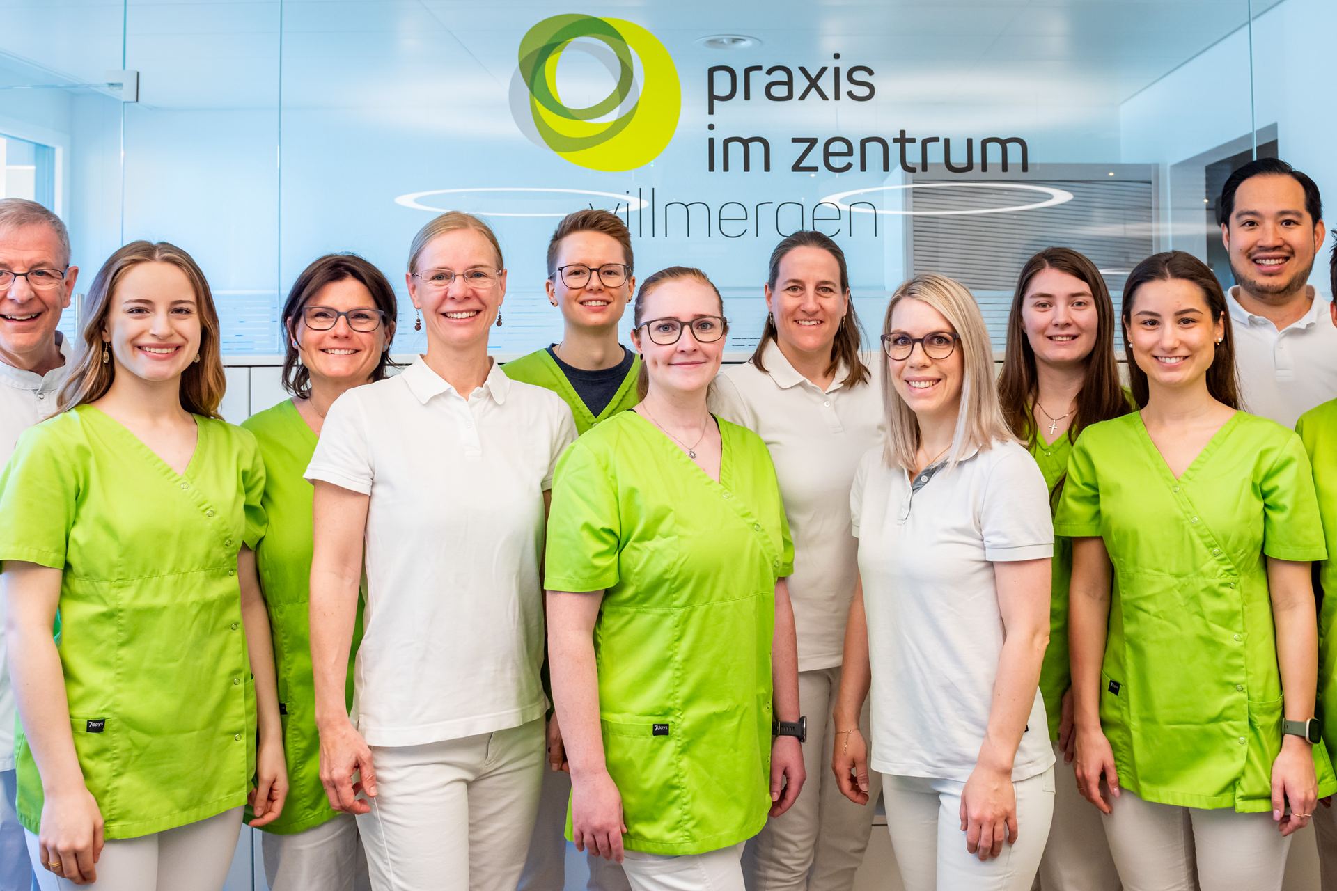 Das Team der Praxis im Zentrum Villmergen vor dem Logo im Empfangsbereich