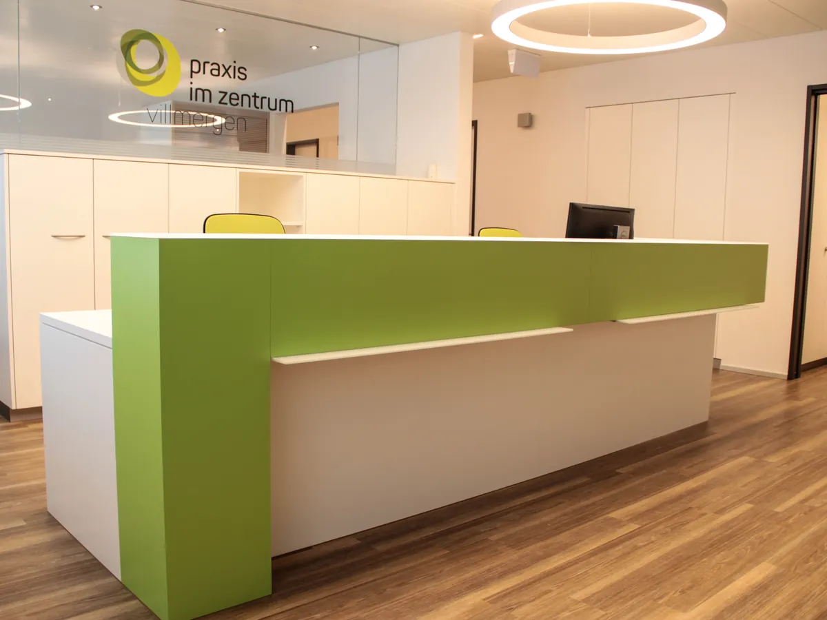 Empfang der Praxis im Zentrum Villmergen mit grünem Tresen und dem Logo an der Glaswand